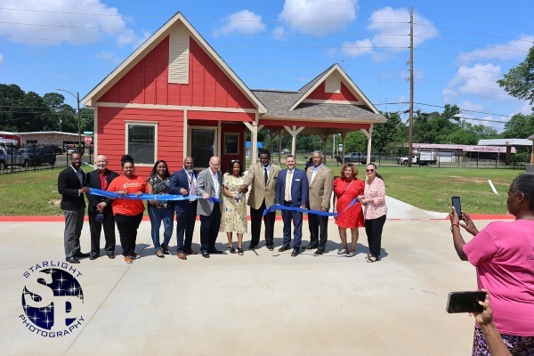 A group of people stand in front of a house to cut a giant ribbon.